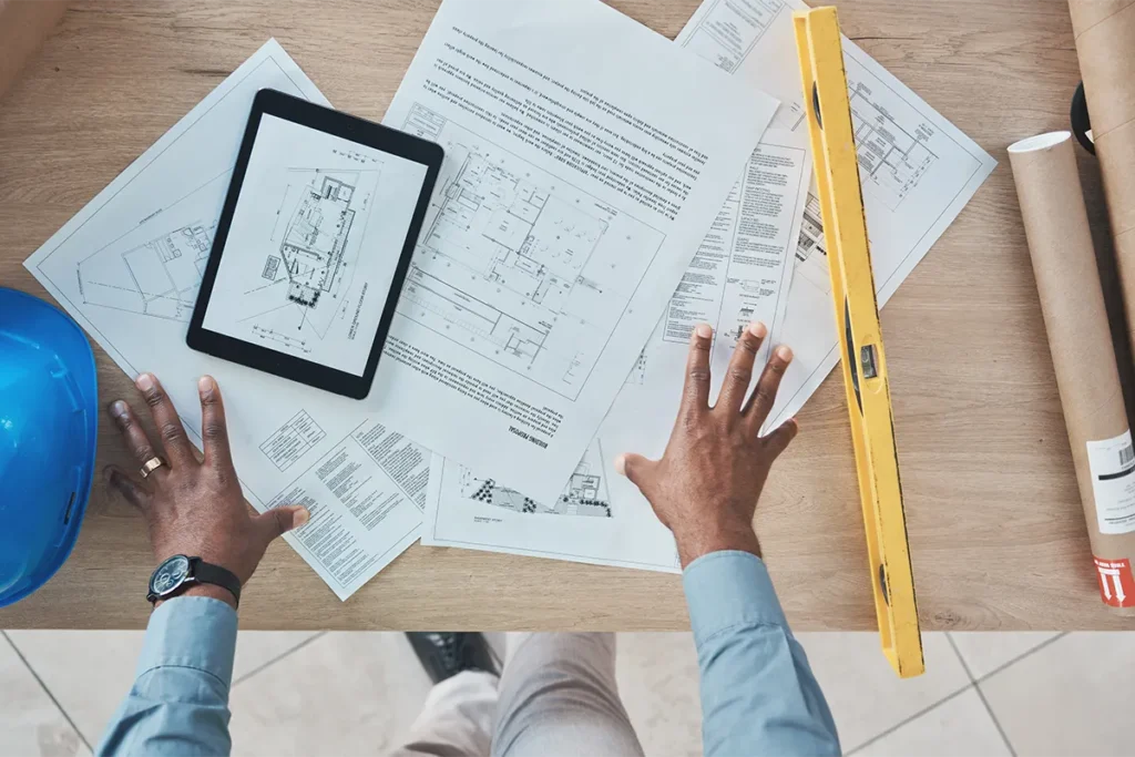 worker standing over desk looking at design plans and blueprints